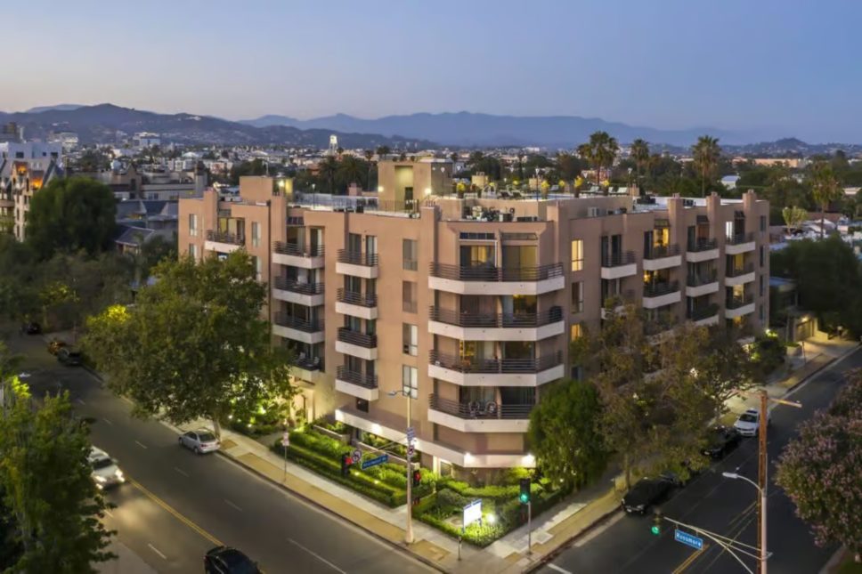 Francis Property Management Aerial view of Chelsea Court Apartments at dusk, nestled in Hancock Park, California. Surrounded by trees and nearby roads with light traffic, the cityscape and distant mountains create a picturesque background.